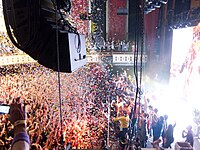 Confetti falling on a packed theater as many people on stage wave to the audience.