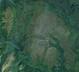 An overhead view of vegetated terrain with two very large, rocky mountains near the crest of a mountain range to the southwest.