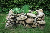 Raised garden bed with natural stones of Salvia, Chives, and Parsley.