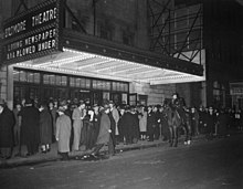 A crowd on the sidewalk in front of the lighted marquee of the Biltmore Theatre