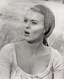 A black-and-white photograph of a woman wearing a headscarf, staring off to the side with her mouth agape.