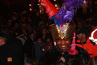 A grinning black man in a turban with feathers.