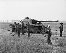 Royal Engineers sweep for mines around a destroyed German tank