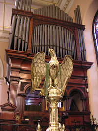 The brass lectern is in the traditional form of an eagle and the organ pipes are shown behind it.