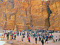 A large variety of people taking photographs of something just beyond the camera, in a canyon with a rocky rear wall (from Tourism in Jordan)