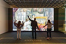Three museum visitors strike different poses as they interact with a digital ARTLENS display.