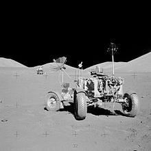 Black and white photo of a lunar rover with a lunar landing module in the background.
