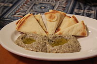 Baba ghanoush is a Levantine dish of cooked eggplant mixed with onions, tomatoes, olive oil and various seasonings, served here with pita bread.