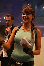 A half-body picture of a brunette woman dressed in a light blue, sleeveless shirt holding a stack of papers.