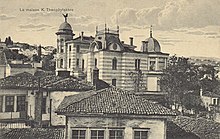 Sepia photograph of a mansion among smaller houses in a city.