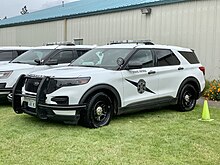 A white Ford Explorer-style SUV with Washington State Patrol markings. Outfitted with law enforcement accessories such as an emergency light bar, spotlight, and push bar.