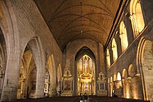 Photographie d'une nef d'église prise en direction du chœur, avec un mur à droite et des arcades à gauche