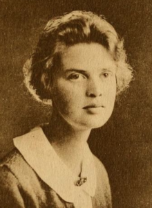 a young white woman with short wavy fair hair, wearing a stiff round white collar pinned at the throat
