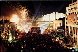 Night view of plaza with crowds and fireworks.