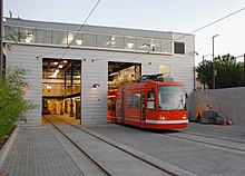 A red streetcar entering a gray, metal building that is lit from the inside.