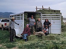 A group of people pose for a photo in a field, in and around a trailer with hay bales