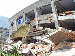 A collapsed structure being bulldozed, with a exposed mountain face in the background