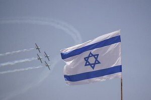 Four aircraft fly in formation as an Israeli flag is visible facing towards the sky