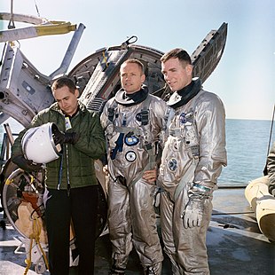 Three men, two of them in space suits, standing on a vessel