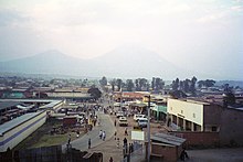 Photograph of Ruhengeri, Rwanda, with buildings, a street, and people visible, and mountains in the background, partially in cloud