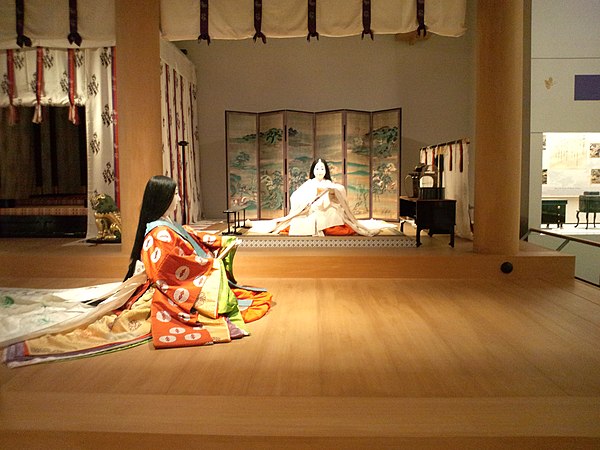 Reconstruction of the interior furnishings of the same building. The Saiō sits on a dais, with a byōbu behind her, a kichō to her left, and a boxlike chōdai (帳台, baldachin) to her right. Above and before her, a kabeshiro (壁代, wall-curtain) is rolled and tied up.