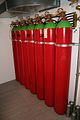 seven large red cylinders, with green tops, side by side in a rack