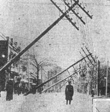 A man stands in the middle of a street while pole lines lean over him.