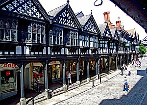 A terrace of shops seen from an angle. The upper storeys are timber-framed with gables; the shops at ground floor level are set back behind an arcade with supporting columns.