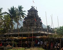 Large, grey temple surrounded by people, palm trees and other vegetation