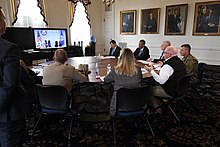 Larry Hogan sits at a round table with members of his administration on a conference call with White House officials about the COVID-19 pandemic. On the television screen is President Donald Trump and Vice President Mike Pence.
