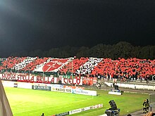 Football fans holding red and white banners in a stadium to form a colourful patern
