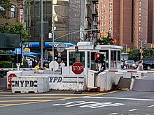An NYPD mobile traffic barrier, showing booth for officers to sit inside of, and the barrier rotated into the blocking position.