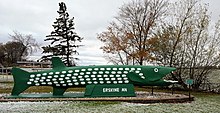 large concrete statue of a northern pike fish in front of a lake