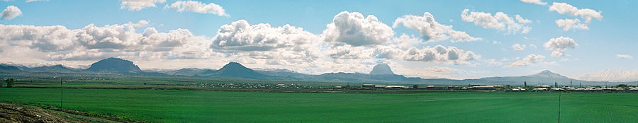a vast green plain with isolated mountains in the distance