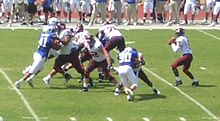 Players clash at the line of scrimmage as a quarterback prepares to pass a ball