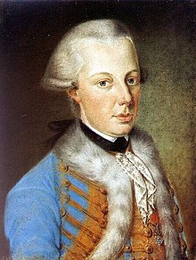 Upper body of a young man wearing a white powdered wig. His eyes are light blue, almost gray. He's wearing a blue Hungarian-style coat lined with fur.