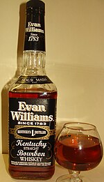 A color photograph of a bottle of bourbon to the left of a glass containing some of that bourbon