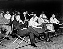 A group of men in shirtsleeves sitting on folding chairs