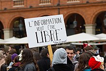 Image of a large crowd, with one sign in the center of the image. The sign reads “Information Wants to be Free” in French.