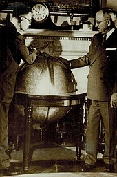 Smith (wearing glasses) and Truman lean over a large globe. A clock on the mantelpiece behind the globe indicates that it is ten o'clock.