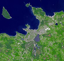 Satellitenaufnahme von der Stadt mit einer großen Wasserfläche in der Stadt. Die umliegenden Orte, das Meer und die linke Insel sind gut zu erkennen.