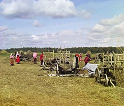 Haymaking farm workers standing near their equipment, taking a break, 1909