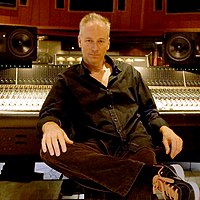Man with black buttoned shirt is sitting on a chair in front of a recording studio