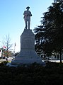 A statue of a Confederate soldier in the town square park is shown. The pedestal reads: "Erected by The Daughters of the Confederacy to the Confederate Soldiers of Macon County".