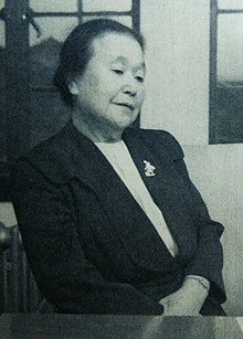 An older Japanese woman, wearing a dark suit