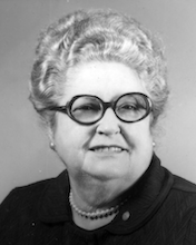image of a white older woman with hair piled on her head in a black shirt. She is wearing glasses