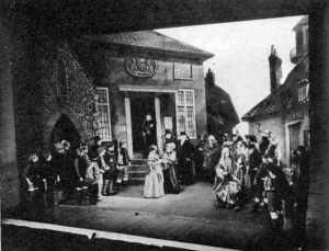 stage scene, showing crowd in the open air with a church and a pub behind them