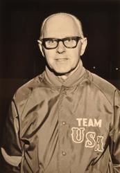 Black and white photo of a aiddle-aged man, balding, wearing thick-rimmed glasses, and a hockey jacket