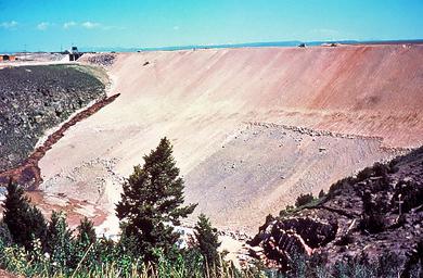 The dark brown streak on the dam face near the gray bedrock in the left half of the photo is a leak that formed on the morning of June 5. The speck above the leak near the top of the dam is a D9 bulldozer on its way to push soil into the leak.