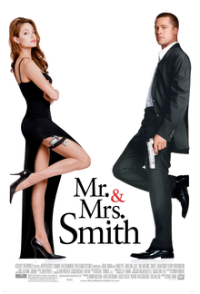 Mr. and Mrs. Smith stand next to a wall, dressed in formal clothing, with Mr. Smith (Brad Pitt) holding a gun on his left hand and Mrs. Smith (Angelina Jolie) having the gun strapped on her right thigh, which is visible. Both look directly at the viewer with the And Symbol (&) painted in red.